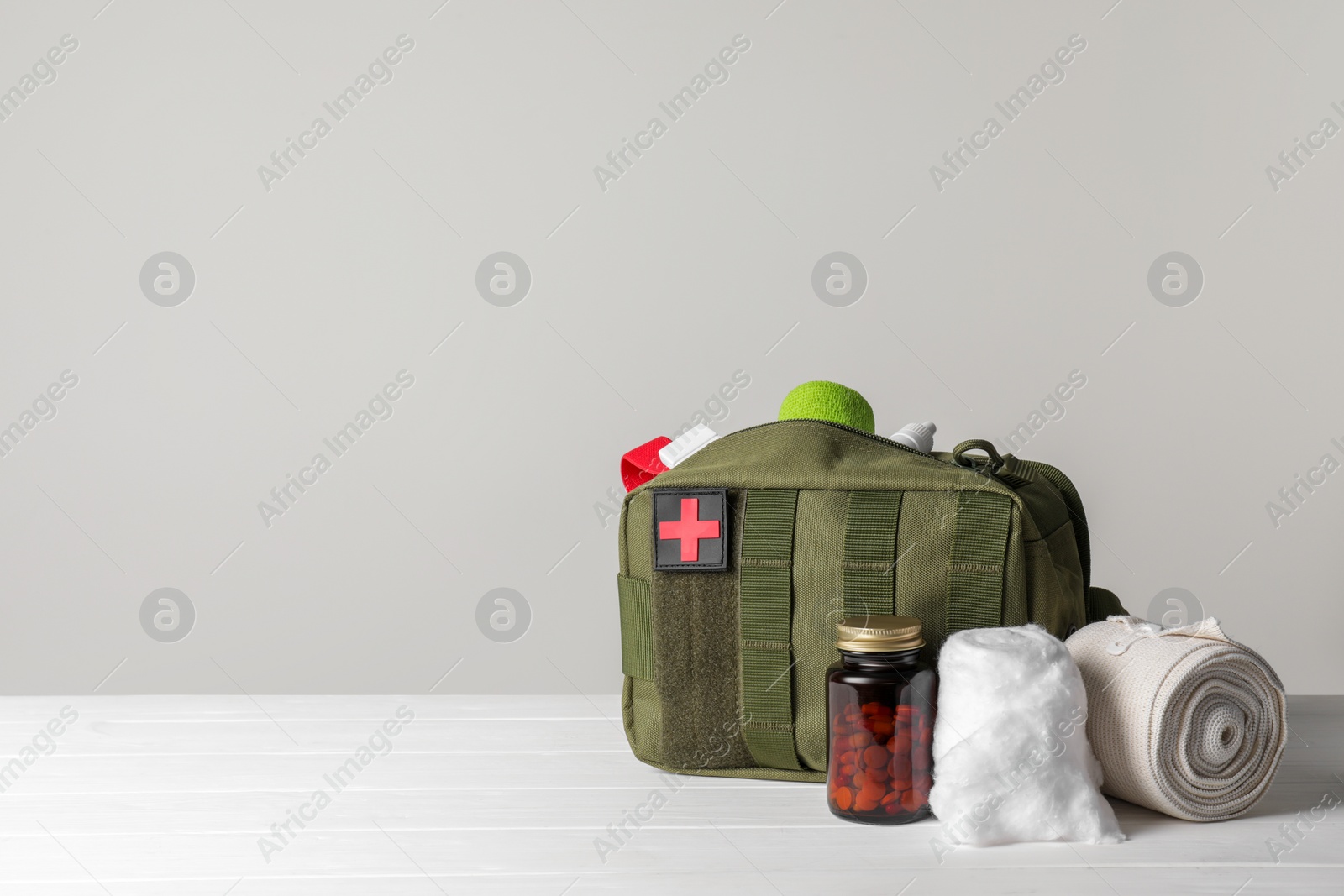 Photo of Military first aid kit, medical cotton, pills and elastic bandage on white wooden table. Space for text