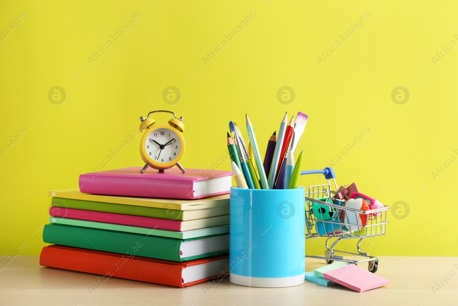 Photo of Different school stationery and alarm clock on table against yellow background. Back to school