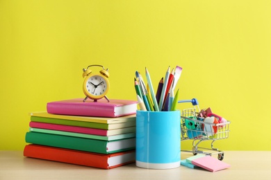 Photo of Different school stationery and alarm clock on table against yellow background. Back to school