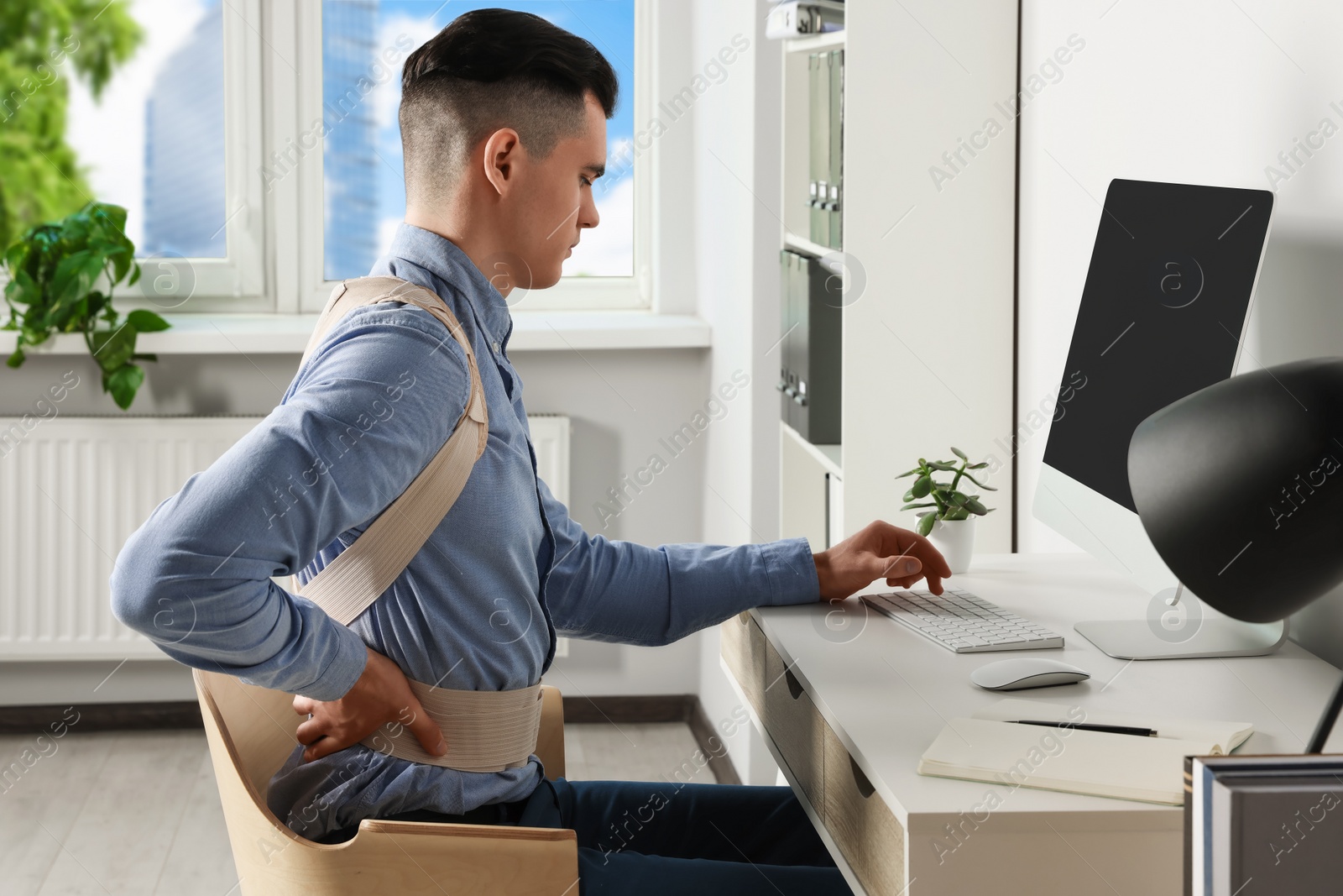 Photo of Man with orthopedic corset working on computer in room