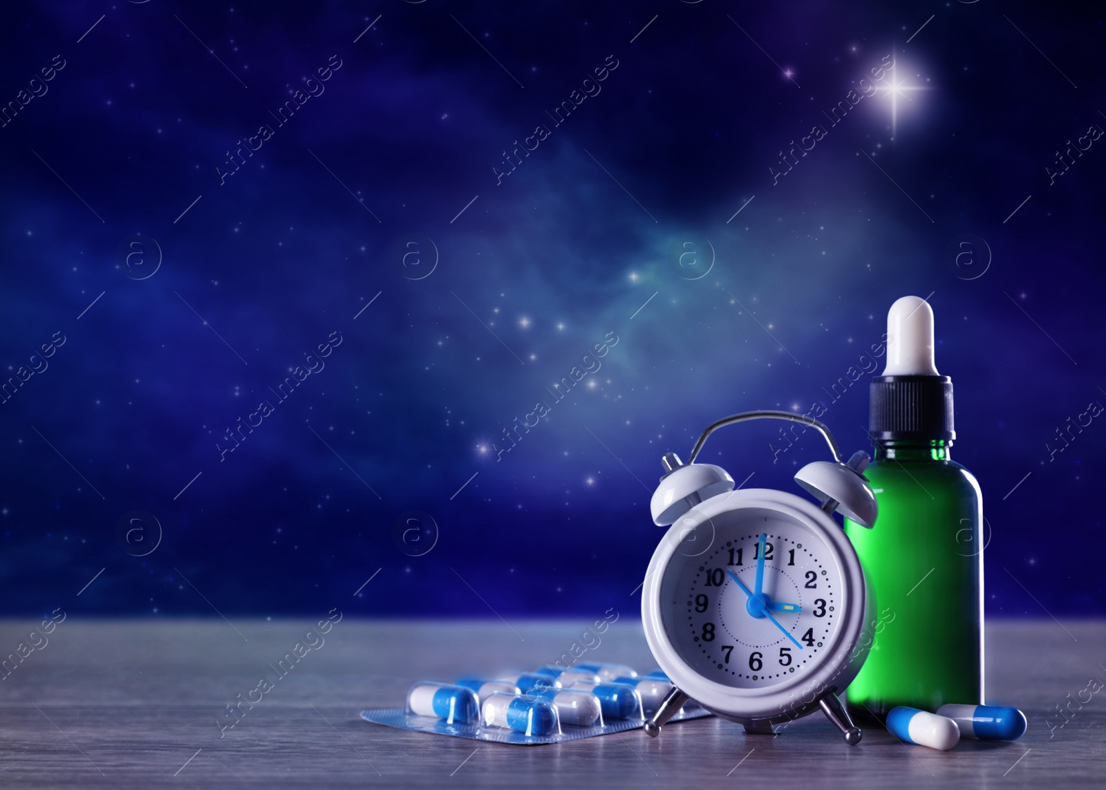 Image of Alarm clock and soporific remedies on wooden table against night sky with stars, space for text. Insomnia