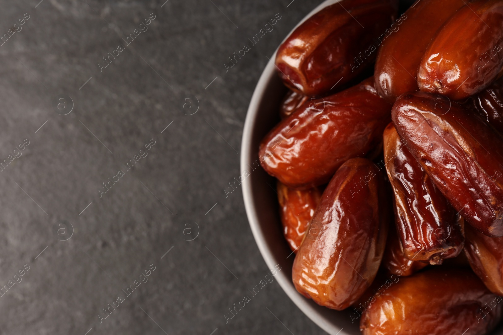 Photo of Tasty sweet dried dates in bowl on black table, top view. Space for text