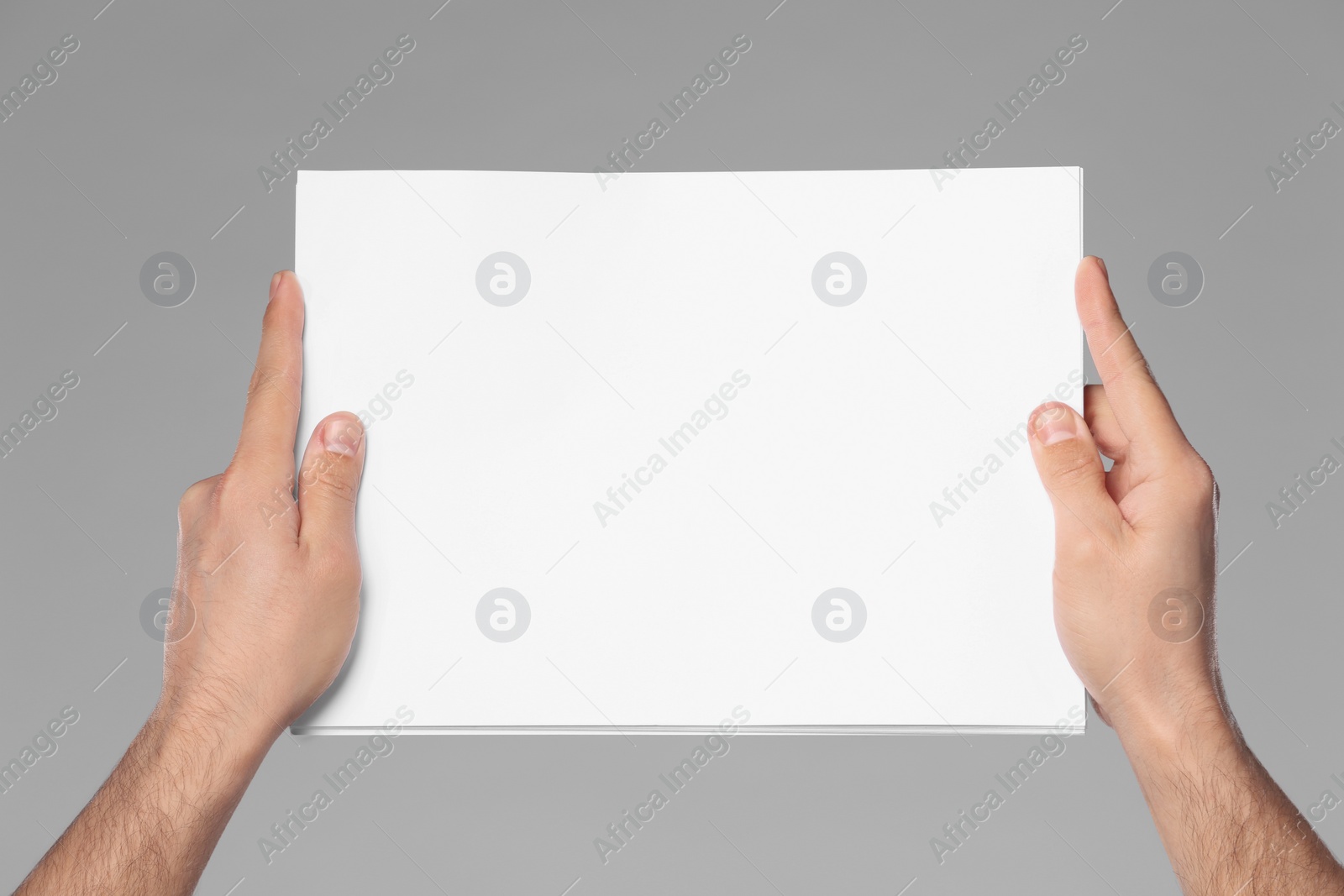 Photo of Man holding sheet of paper on grey background, closeup. Mockup for design