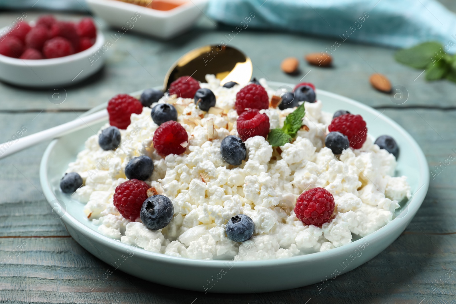 Photo of Delicious cottage cheese with fresh berries served for breakfast on light blue wooden table, closeup