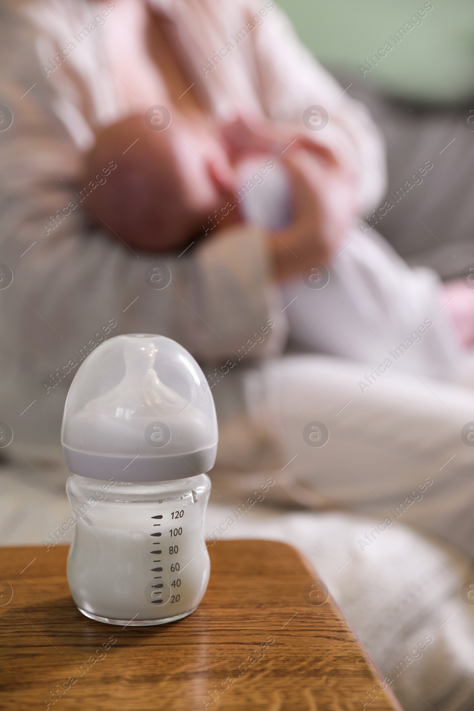 Photo of Mother and her little baby at home, focus on bottle of milk. Space for text