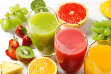 Photo of Glasses with different juices and fresh fruits on wooden table