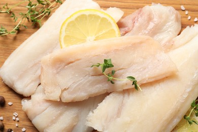 Photo of Pieces of raw cod fish and lemon on wooden table, closeup