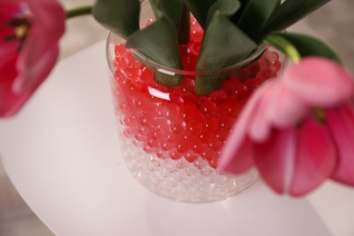 Photo of Different color fillers and tulips in glass vase, closeup. Water beads