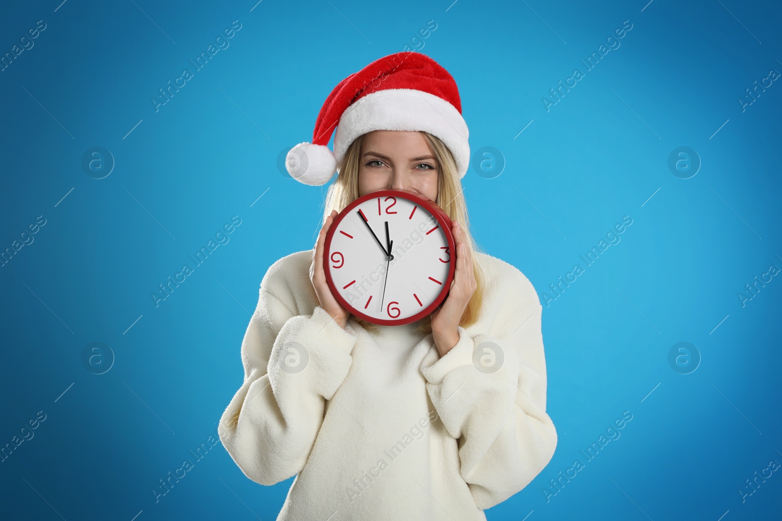 Photo of Woman in Santa hat with clock on light blue background. New Year countdown
