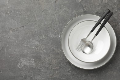 Stylish setting with cutlery and plates on grey textured table, top view. Space for text