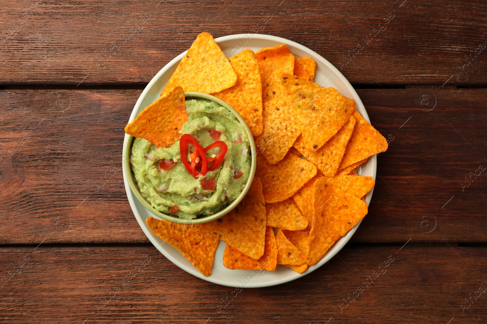 Photo of Bowl of delicious guacamole and nachos chips on wooden table, top view