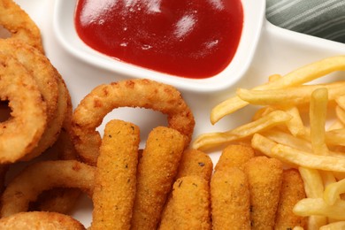 Photo of Tasty ketchup and different snacks on plate, closeup
