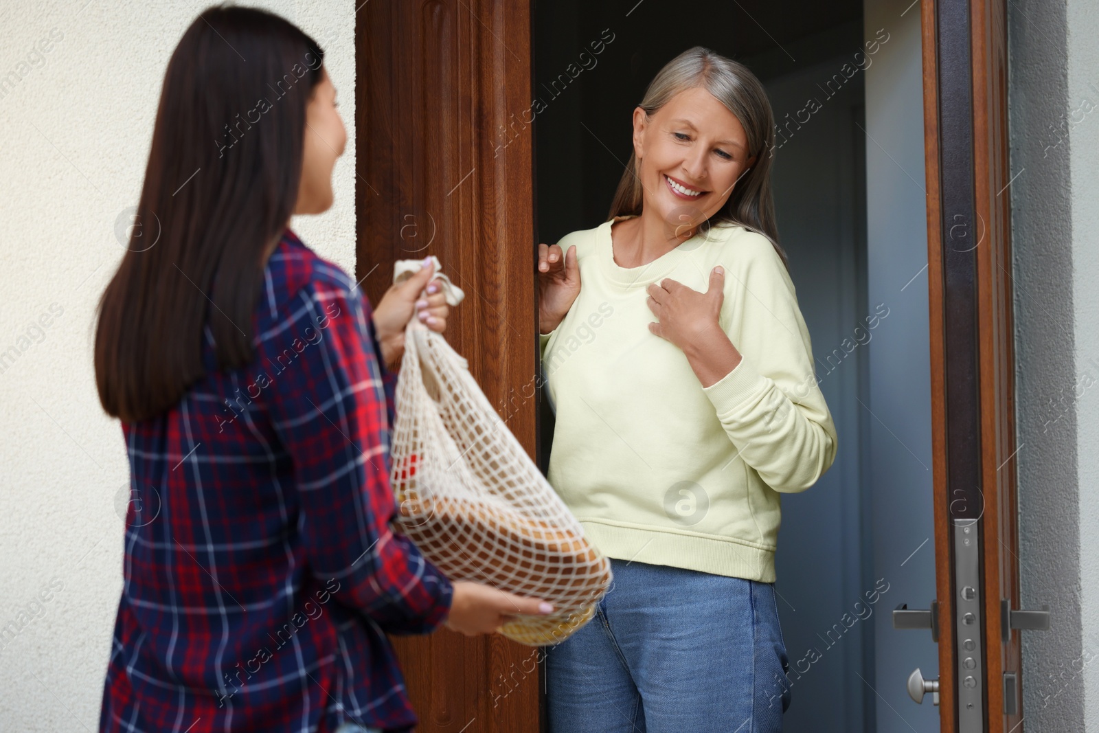 Photo of Young woman with net bag of products helping her senior neighbour outdoors