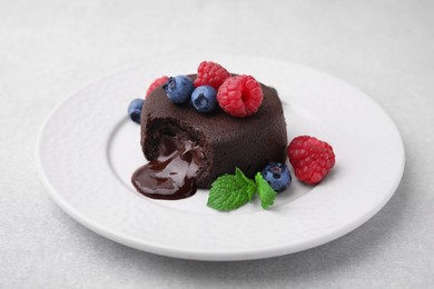 Photo of Plate with delicious chocolate fondant, berries and mint on light grey table