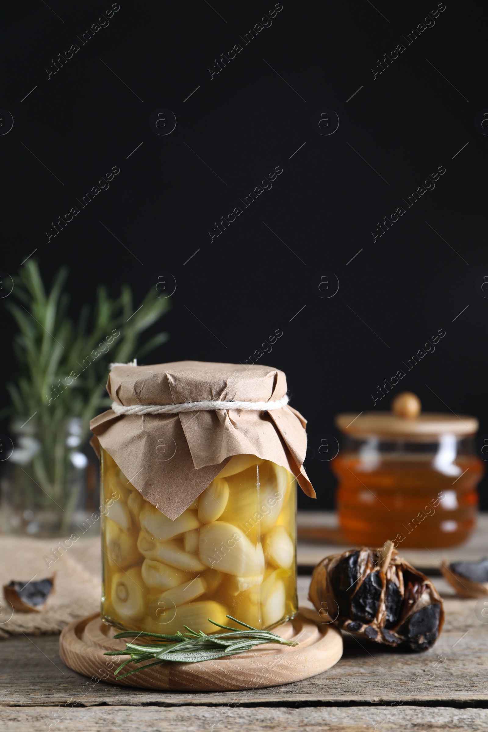 Photo of Garlic with honey in glass jar and fermented black garlic on wooden table