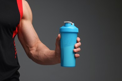 Photo of Young man with muscular body holding shaker of protein on grey background, closeup. Space for text