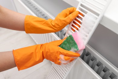 Photo of Woman washing radiator grill with sponge and detergent indoors, closeup