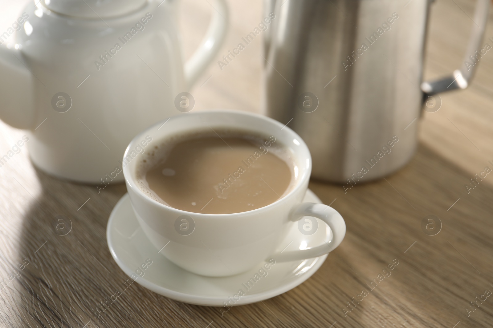 Photo of Aromatic tea with milk in cup, teapot and pitcher on wooden table, closeup