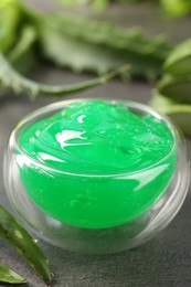 Photo of Bowl with natural gel and aloe vera leaves on grey table, closeup