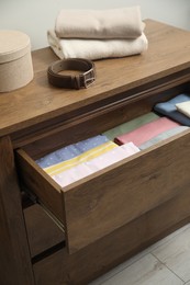 Chest of drawers with different folded clothes and accessories indoors