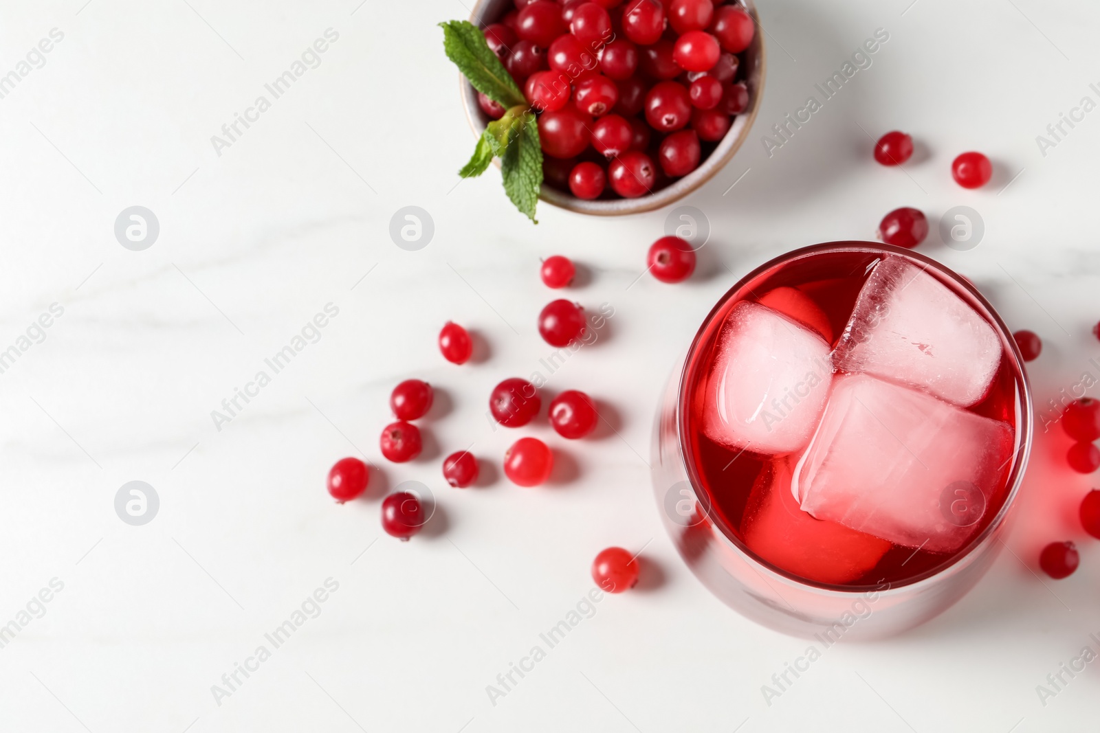 Photo of Tasty cranberry juice with ice cubes in glass and fresh berries on white wooden table, top view. Space for text