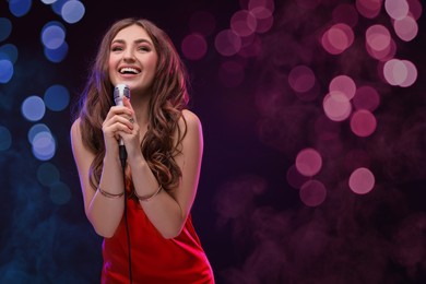 Image of Beautiful woman with microphone singing on stage in color lighted smoke