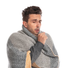 Young man wrapped in warm blanket suffering from cold on white background