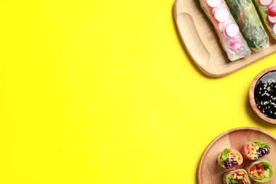 Photo of Different delicious spring rolls and soy sauce on yellow background, flat lay. Space for text