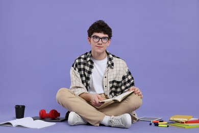 Portrait of student with notebook and stationery sitting on purple background