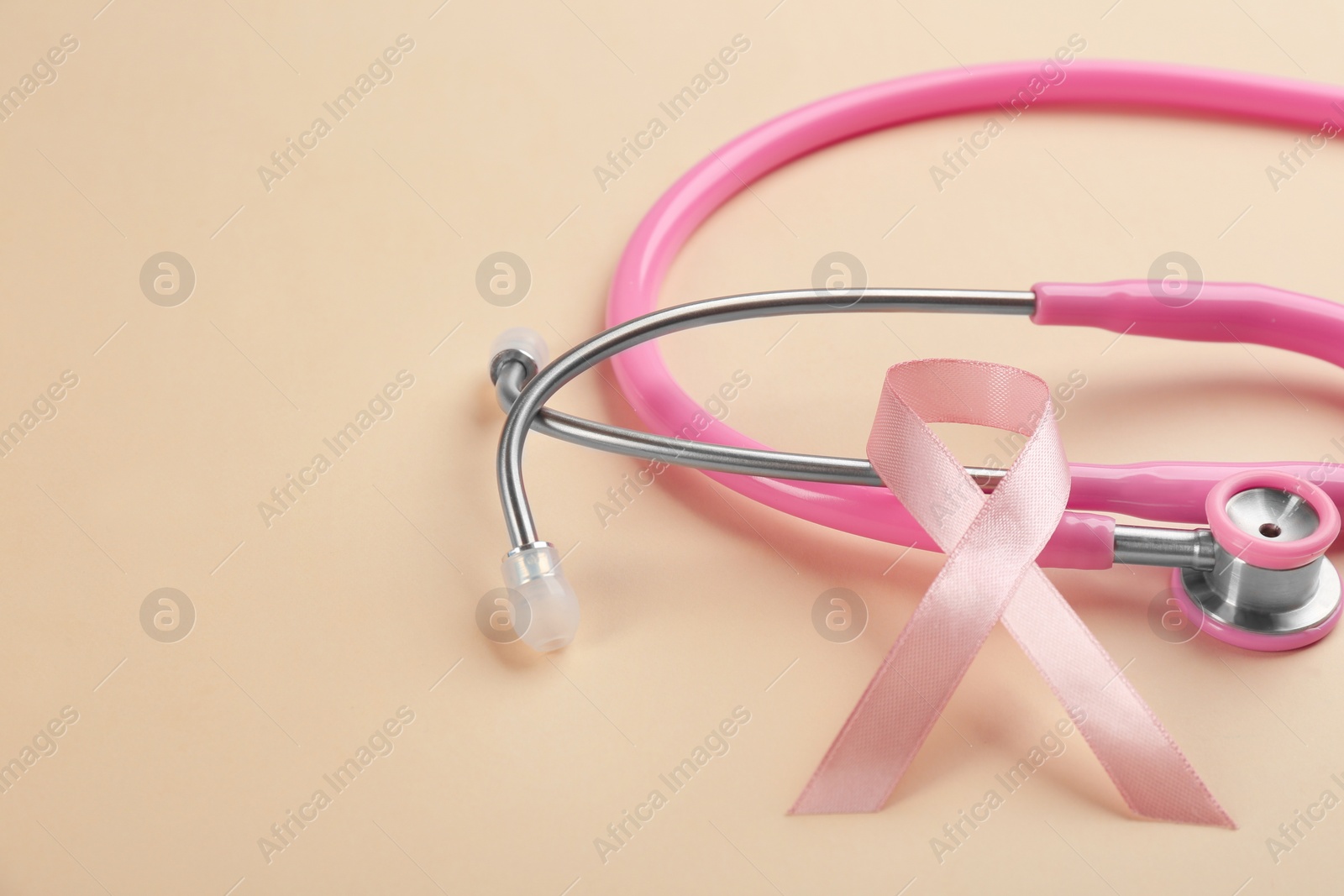 Photo of Pink ribbon and stethoscope on beige background, closeup. Breast cancer concept