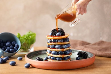 Photo of Woman pouring syrup onto tasty pancakes with berries on plate, closeup