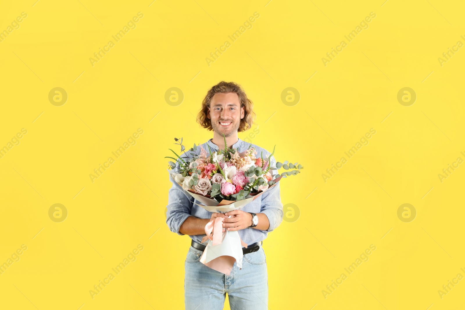 Photo of Young handsome man with beautiful flower bouquet on yellow background