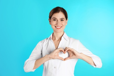 Portrait of woman making heart with her hands on color background