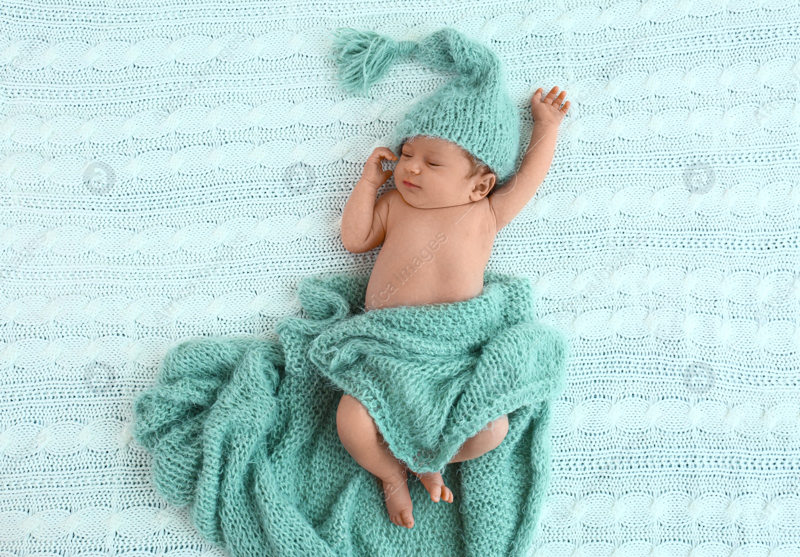 Photo of Cute little baby in green hat lying on soft blanket, top view