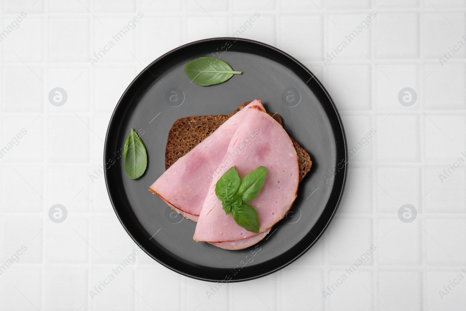 Photo of Delicious sandwich with ham on white tiled table, top view