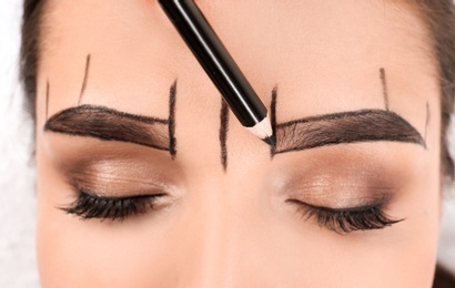 Photo of Cosmetologist preparing young woman for  eyebrow permanent makeup procedure, closeup