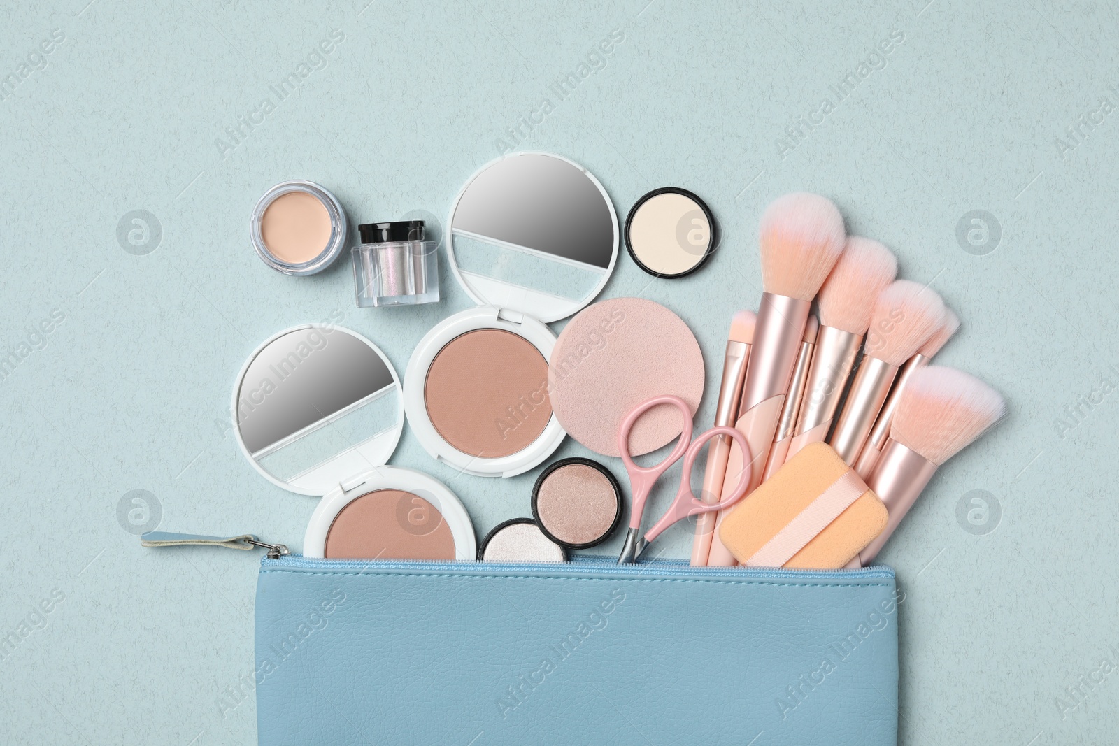 Photo of Cosmetic bag with makeup products and beauty accessories on light blue background, flat lay