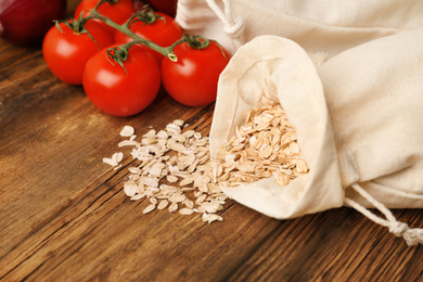 Photo of Cotton eco bags with vegetables and oat flakes on wooden table, closeup