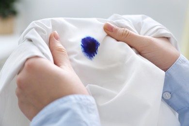 Photo of Woman holding white shirt with blue ink stain on blurred background, closeup