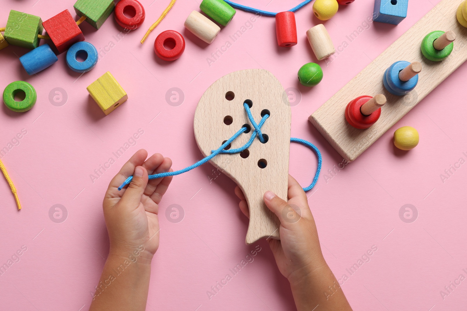 Photo of Motor skills development. Little child playing with wooden lacing toy at pink table, top view