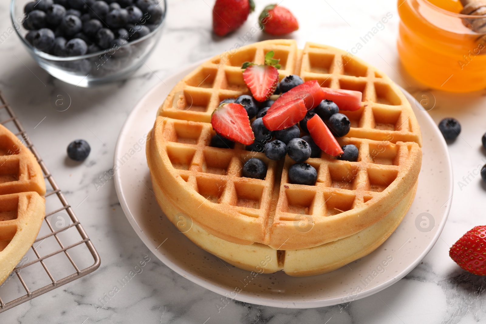 Photo of Tasty Belgian waffles with fresh berries and honey on white marble table, closeup