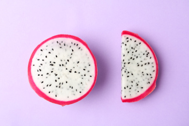 Photo of Slices of delicious dragon fruit (pitahaya) on violet background, flat lay