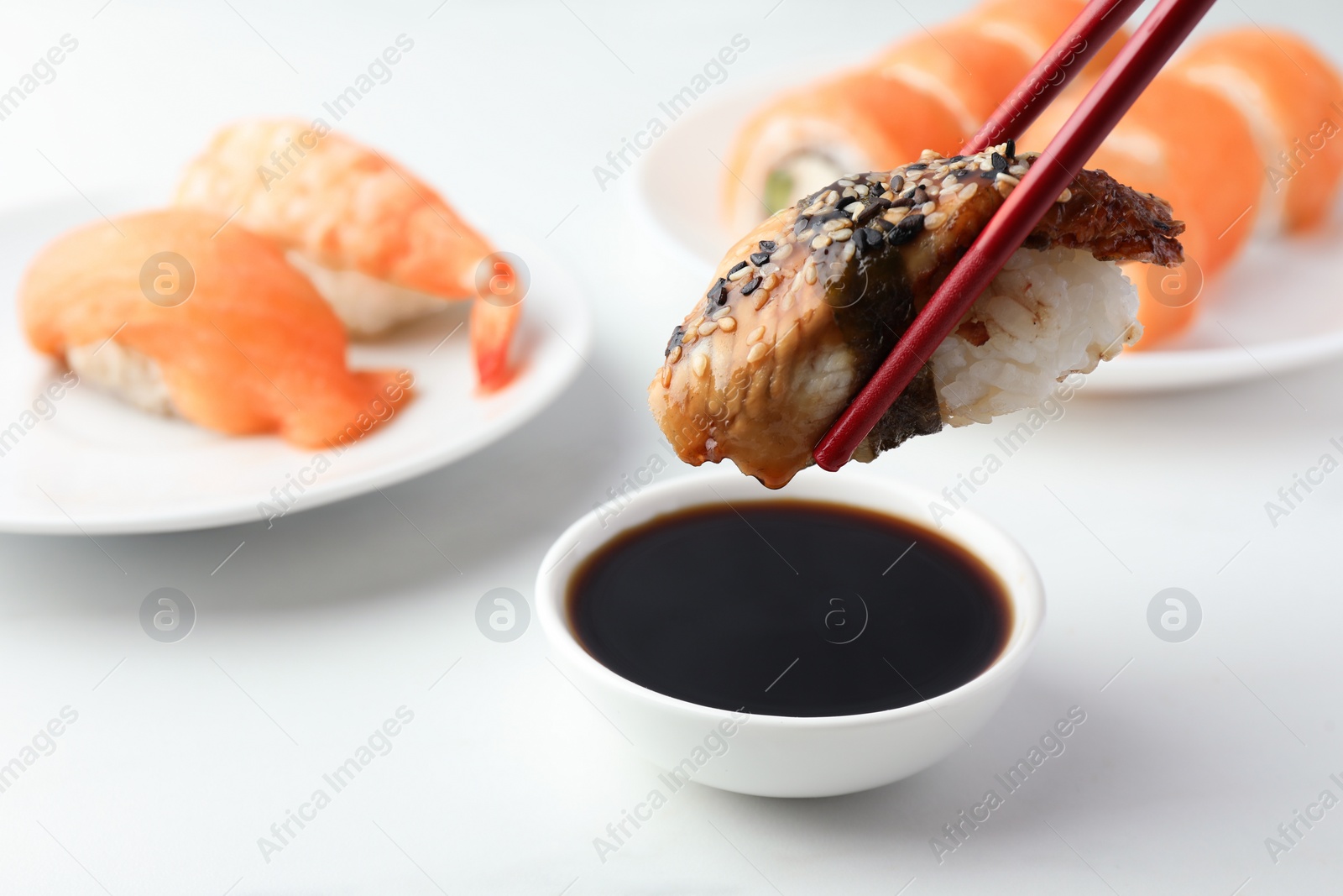 Photo of Dipping tasty nigiri sushi with smoked eel into soy sauce on white table, closeup