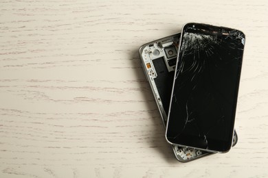 Photo of Damaged smartphone on white wooden table, top view with space for text. Device repairing