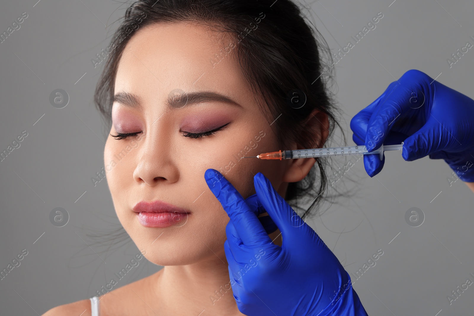 Photo of Woman getting facial injection on grey background