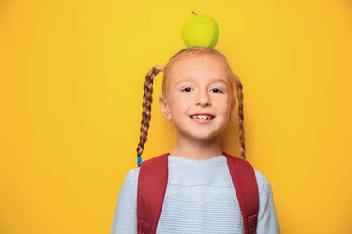 Photo of Funny little girl with backpack and apple on yellow background