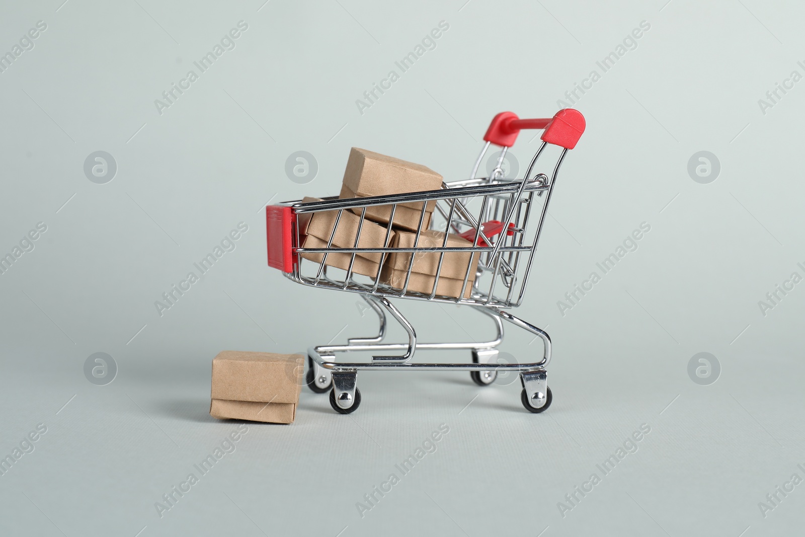 Photo of Small metal shopping cart with cardboard boxes on light background