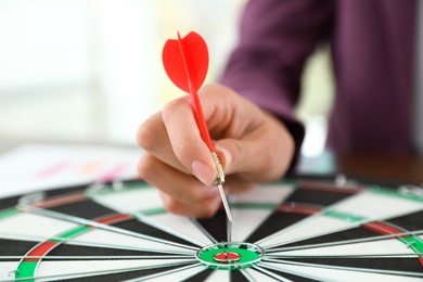 Photo of Businesswoman holding dart over center of board at table, closeup