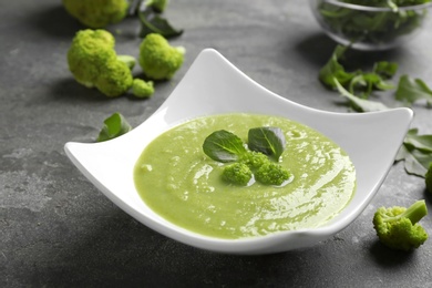 Photo of Bowl of broccoli cream soup on grey table