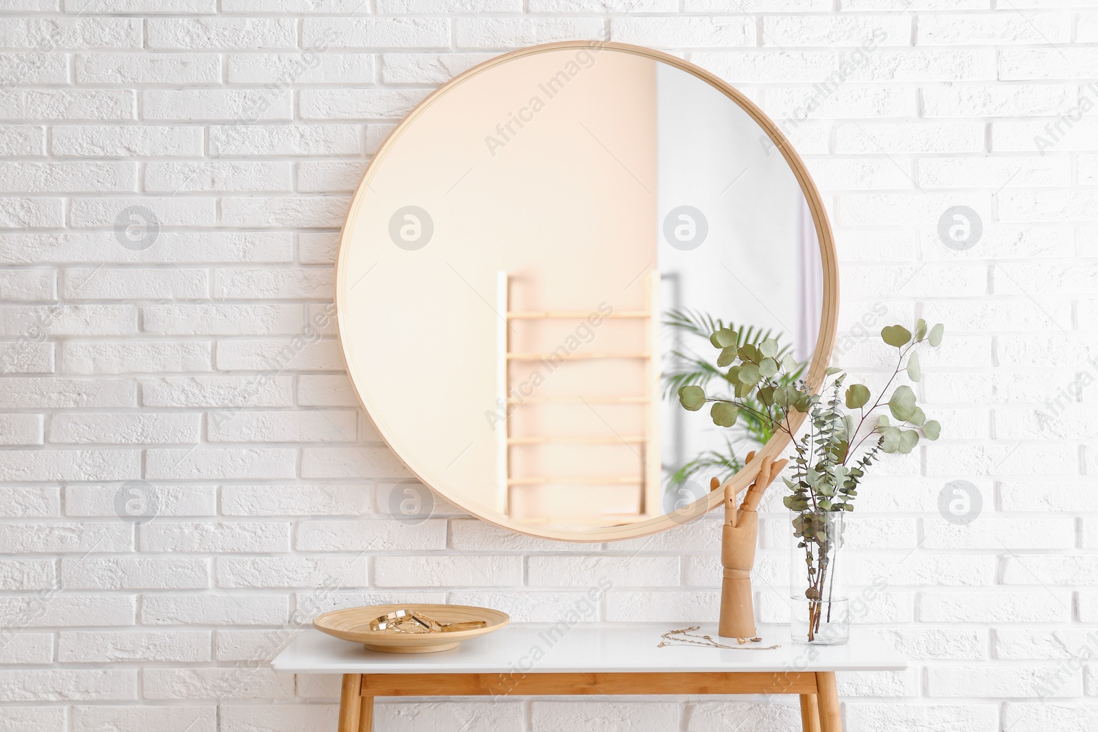 Photo of Big round mirror, table with jewelry and decor near brick wall in hallway interior